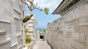 A narrow wooden pathway flanked by concrete walls with a tree branch overhanging on the left.