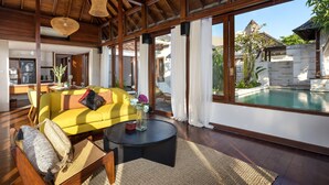 A spacious living area with a yellow sofa, a round coffee table, and a view of a swimming pool.
