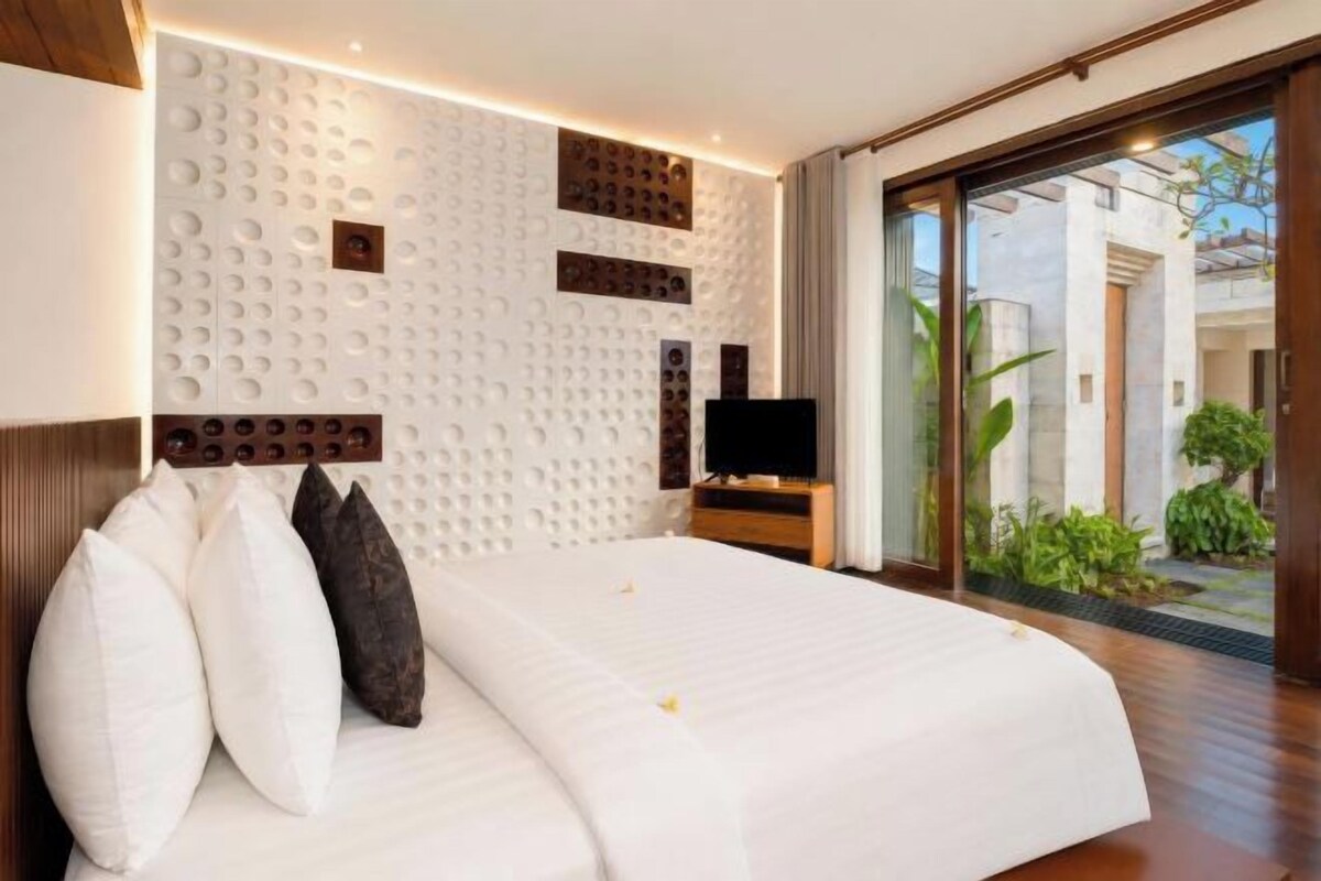 Quarto de hotel com uma cama grande, televisão e porta de vidro deslizante para área externa.