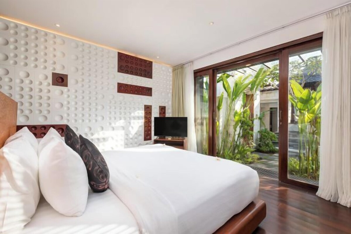 A bedroom with a bed, a television, and a sliding glass door leading to a garden.