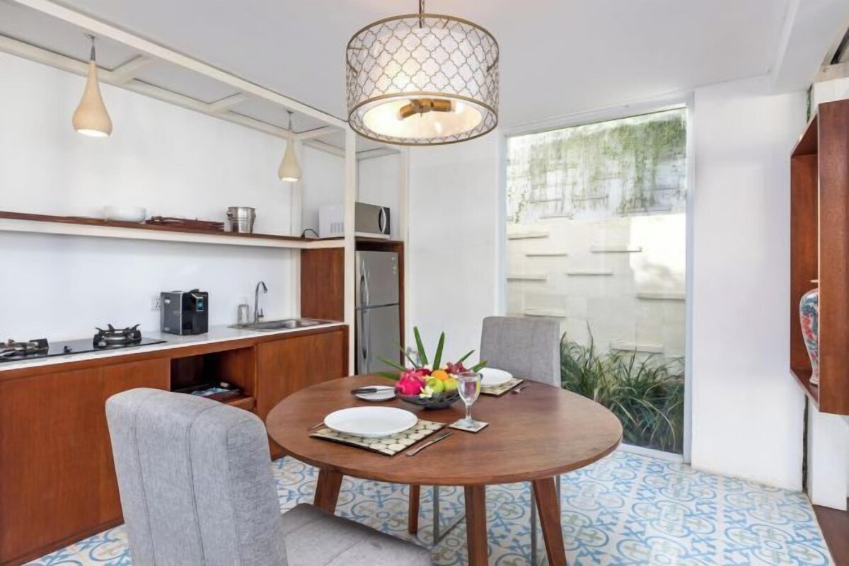 Uma sala de jantar com mesa redonda, cadeiras, um candelabro e vista para o exterior.