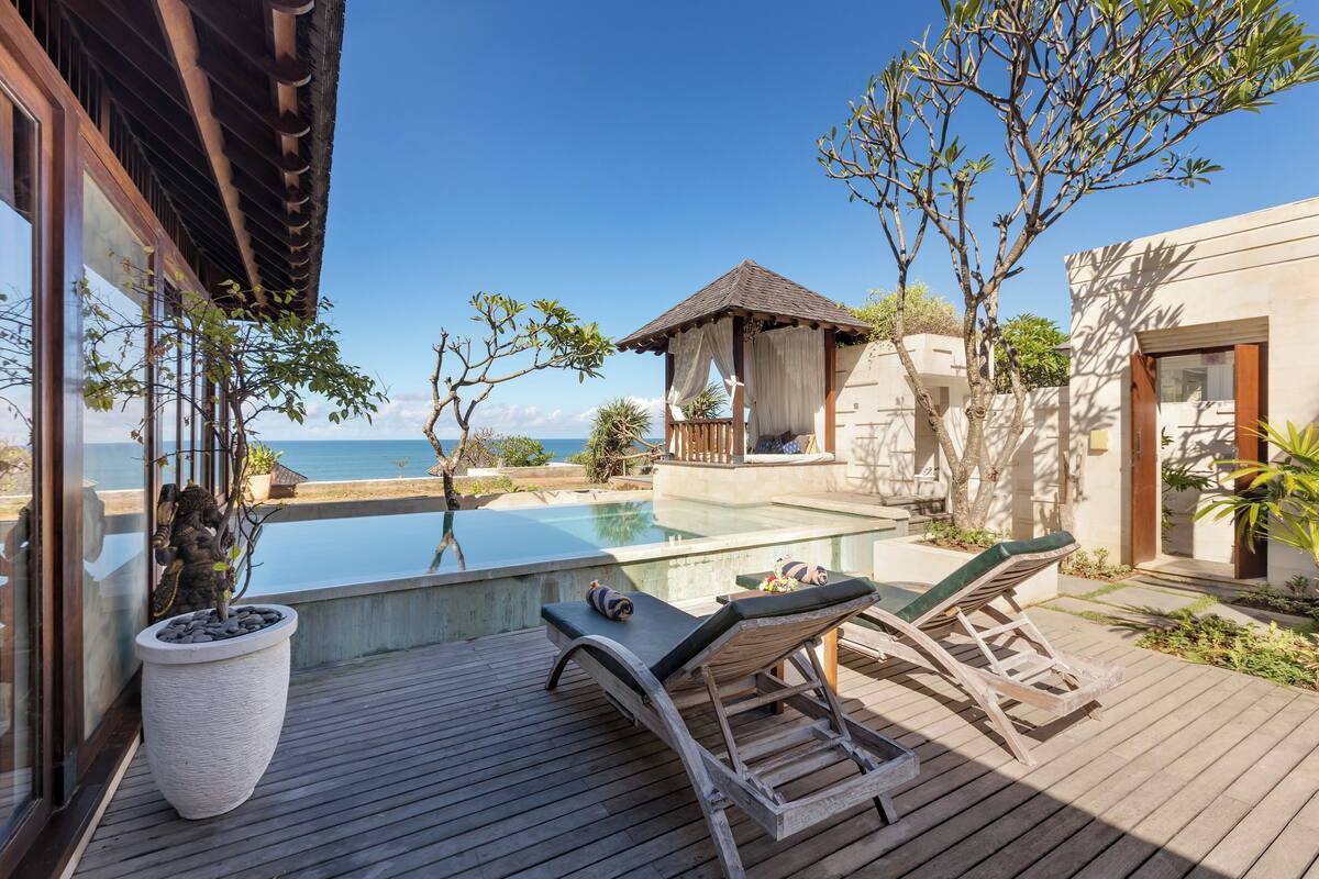 A wooden deck with lounge chairs, a swimming pool, and a view of the sea.