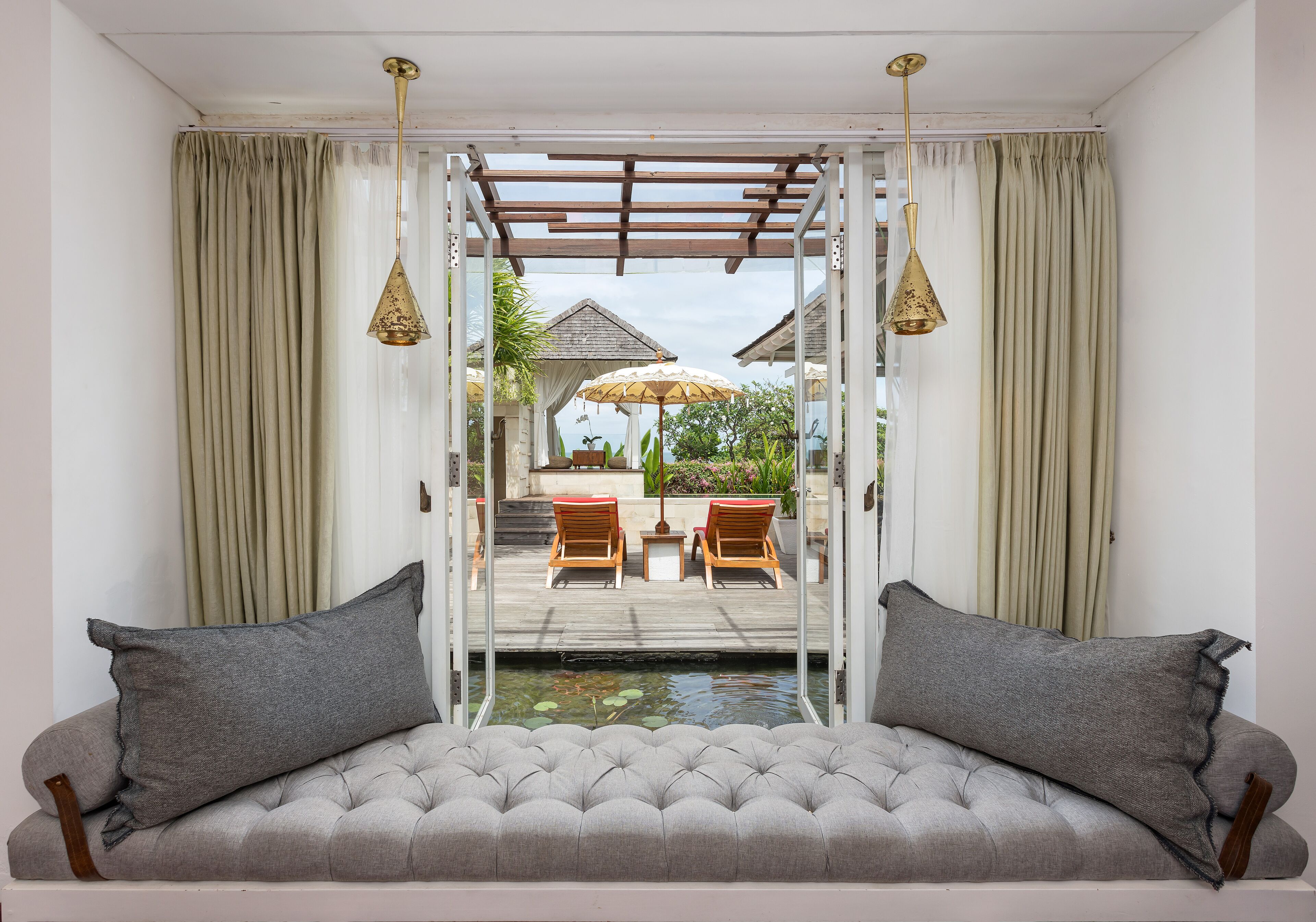 A room with a view of an outdoor patio, a cushioned sofa, and two hanging lamps.