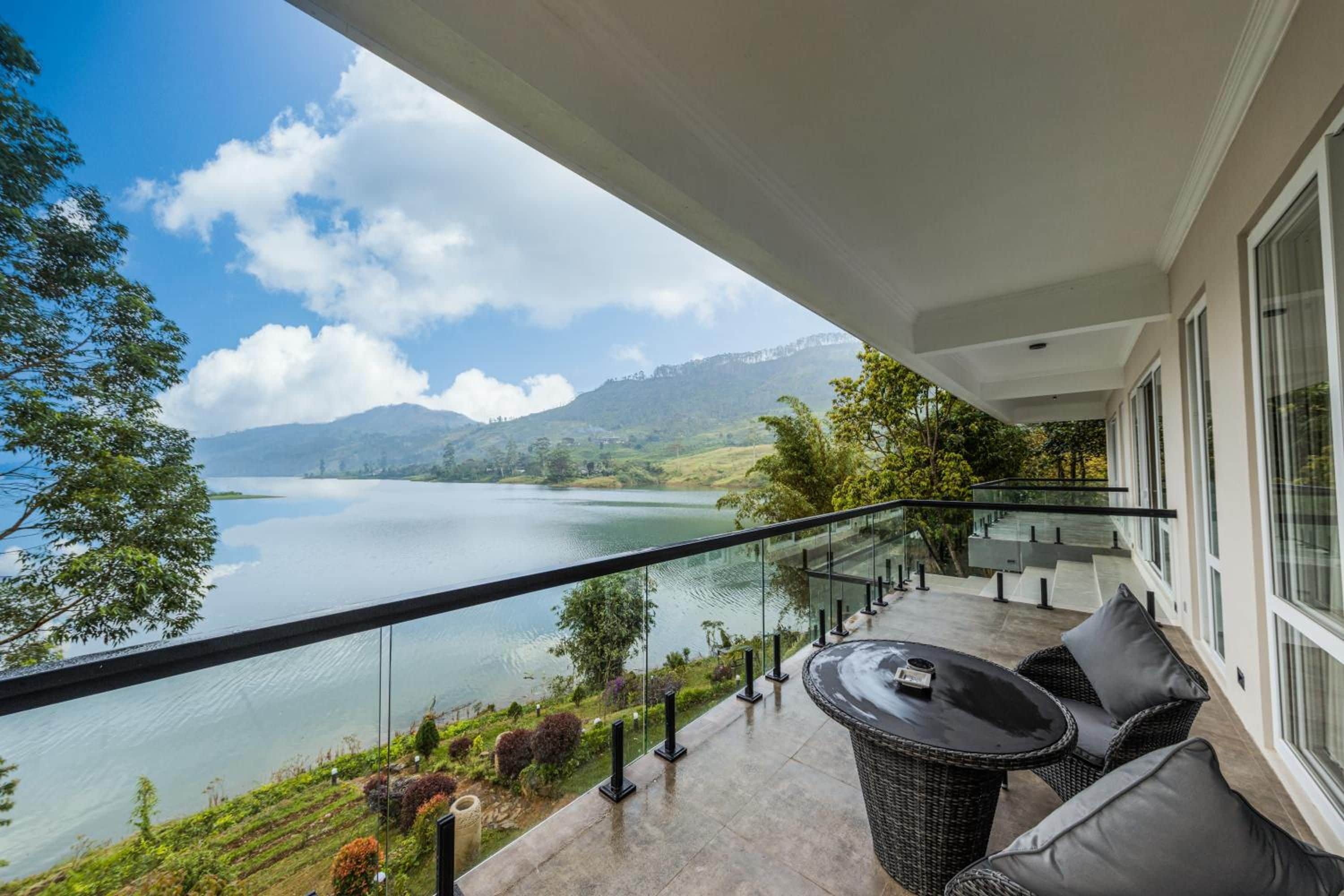 A balcony with a view of a lake and mountains, furnished with a table and chairs.