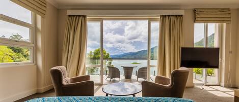 Ett hotellrum med en stor säng, en TV, en balkong med utsikt över havet och bergen samt två stolar.