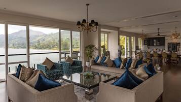 A spacious living room with a large window overlooking a lake and hills, furnished with sofas and a coffee table.