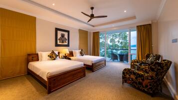 Habitación de hotel con dos camas, ventilador de techo, ventana grande con vistas y un sillón estampado.