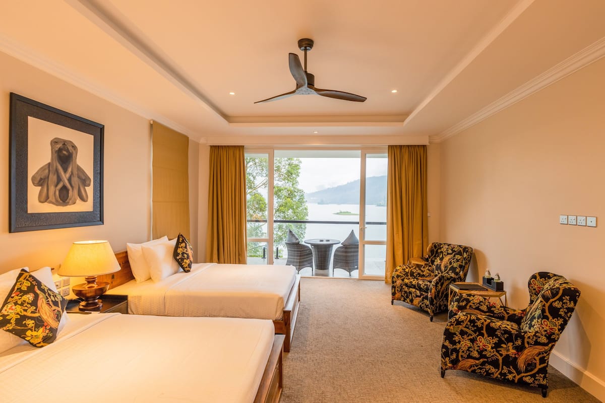 A hotel room with two beds, a ceiling fan, a table with chairs, and a view of the outdoors.