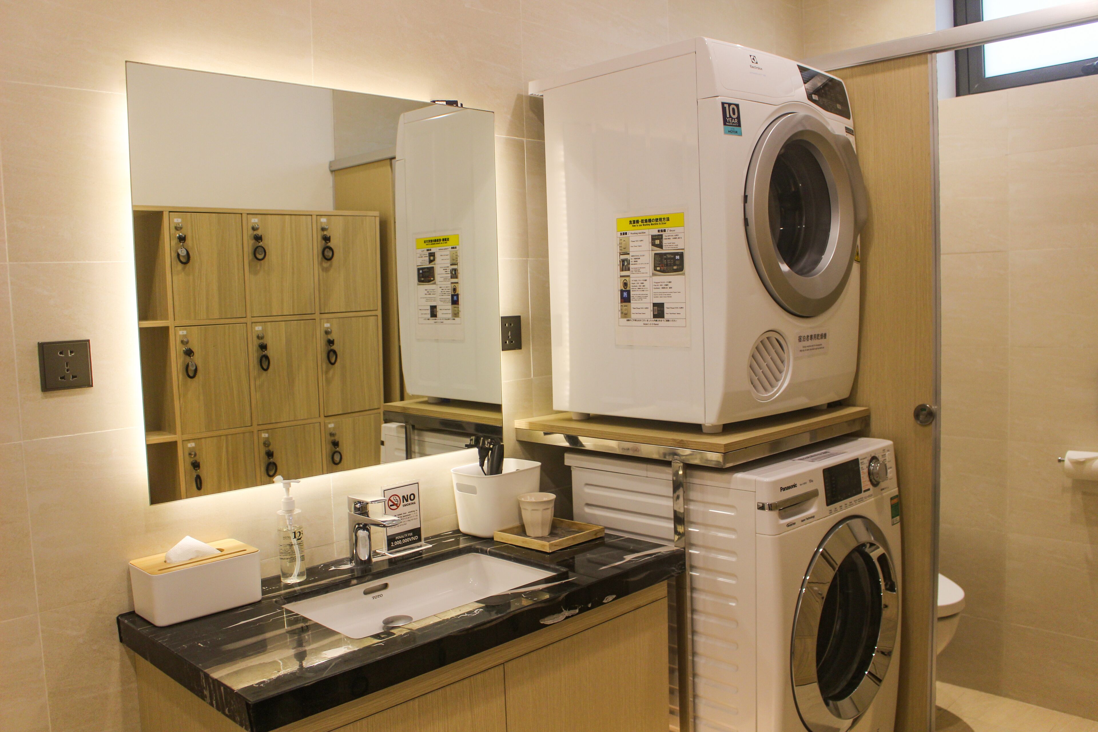 A hotel bathroom with a sink, mirror, wooden cabinets, a washing machine, and a toilet.