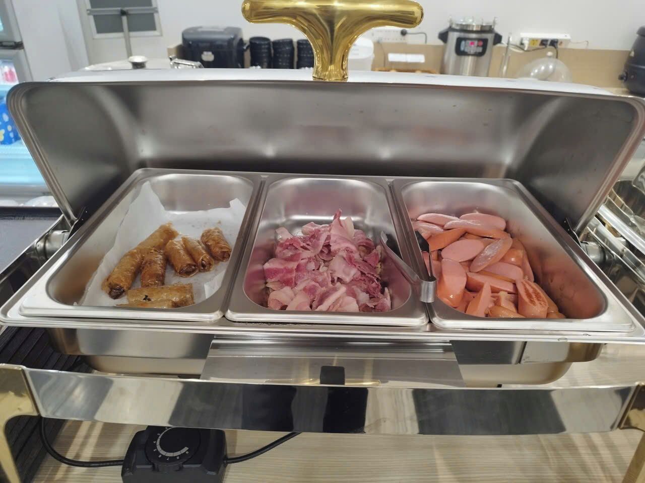 Een buffet met drie schalen eten: worst, plakjes ham en hotdogs.