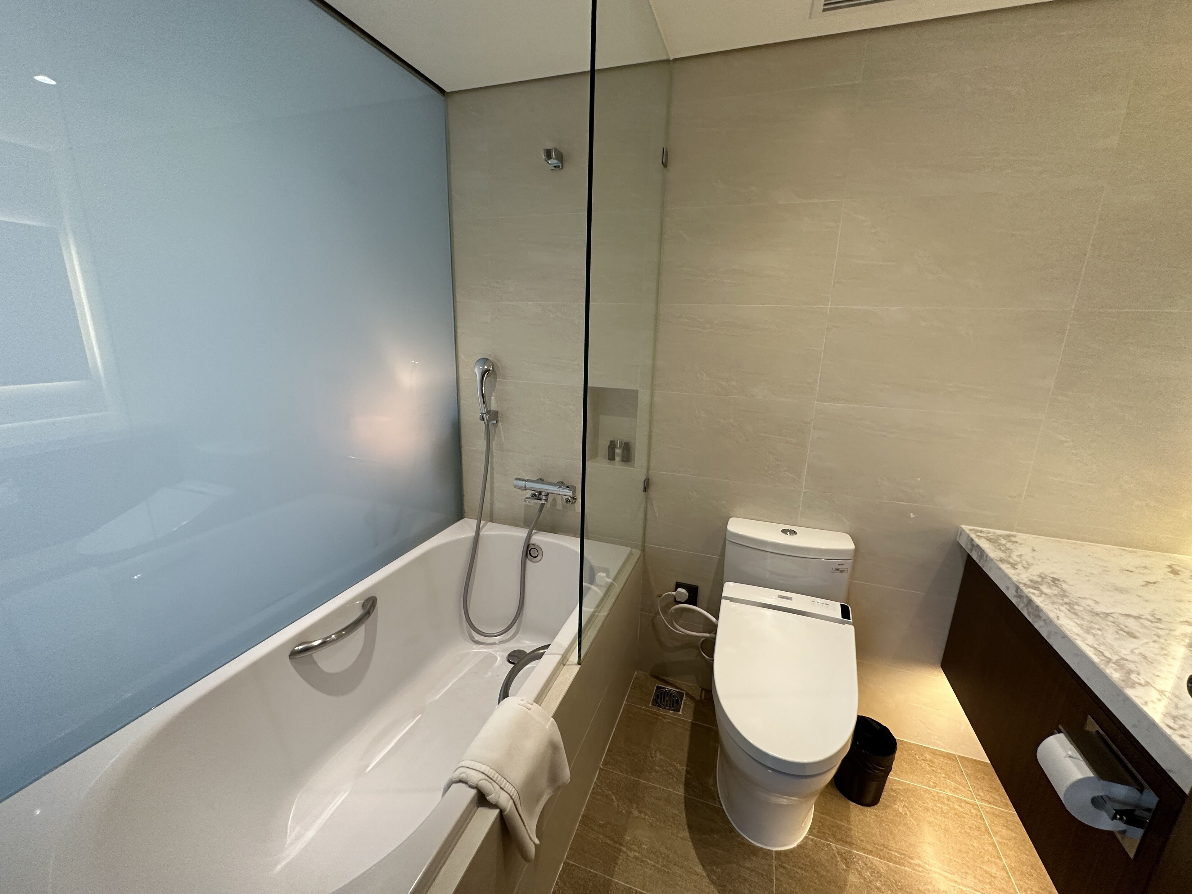 A modern bathroom with a bathtub, toilet, and glass shower enclosure.