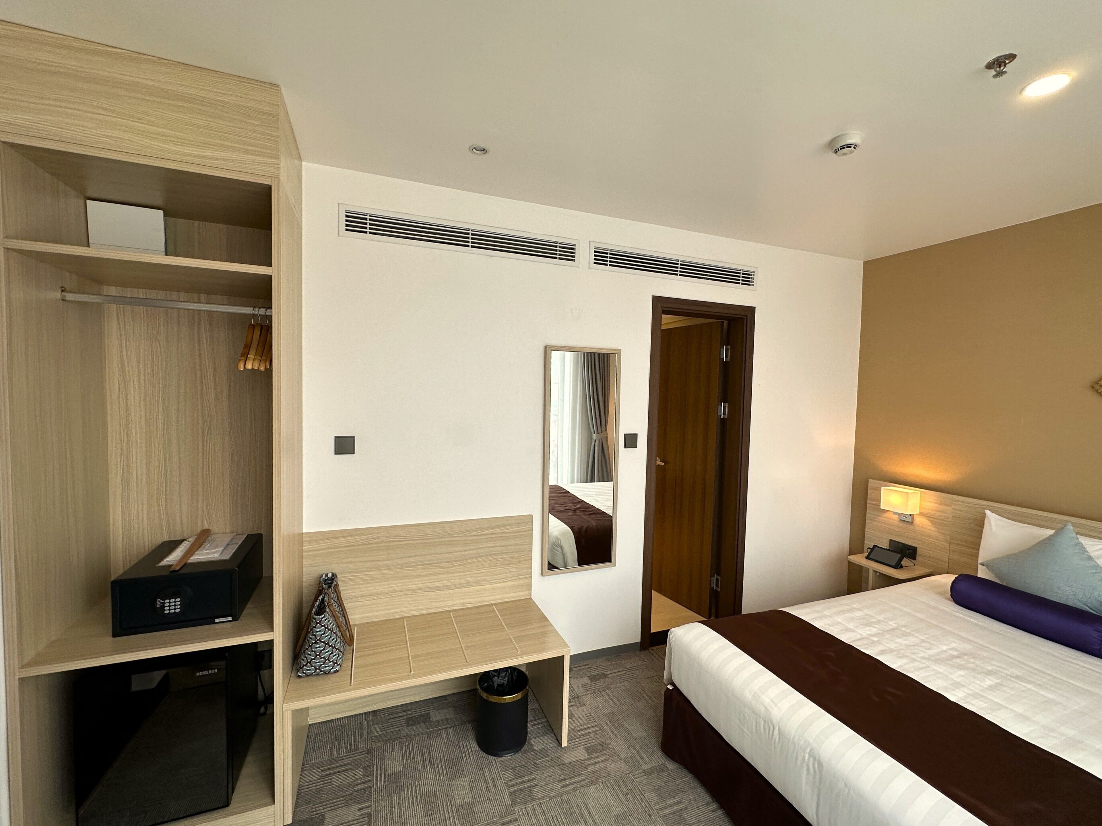 Ein Hotelzimmer mit Bett, Schreibtisch, Kleiderschrank, Spiegel und Nachttisch mit Lampe.