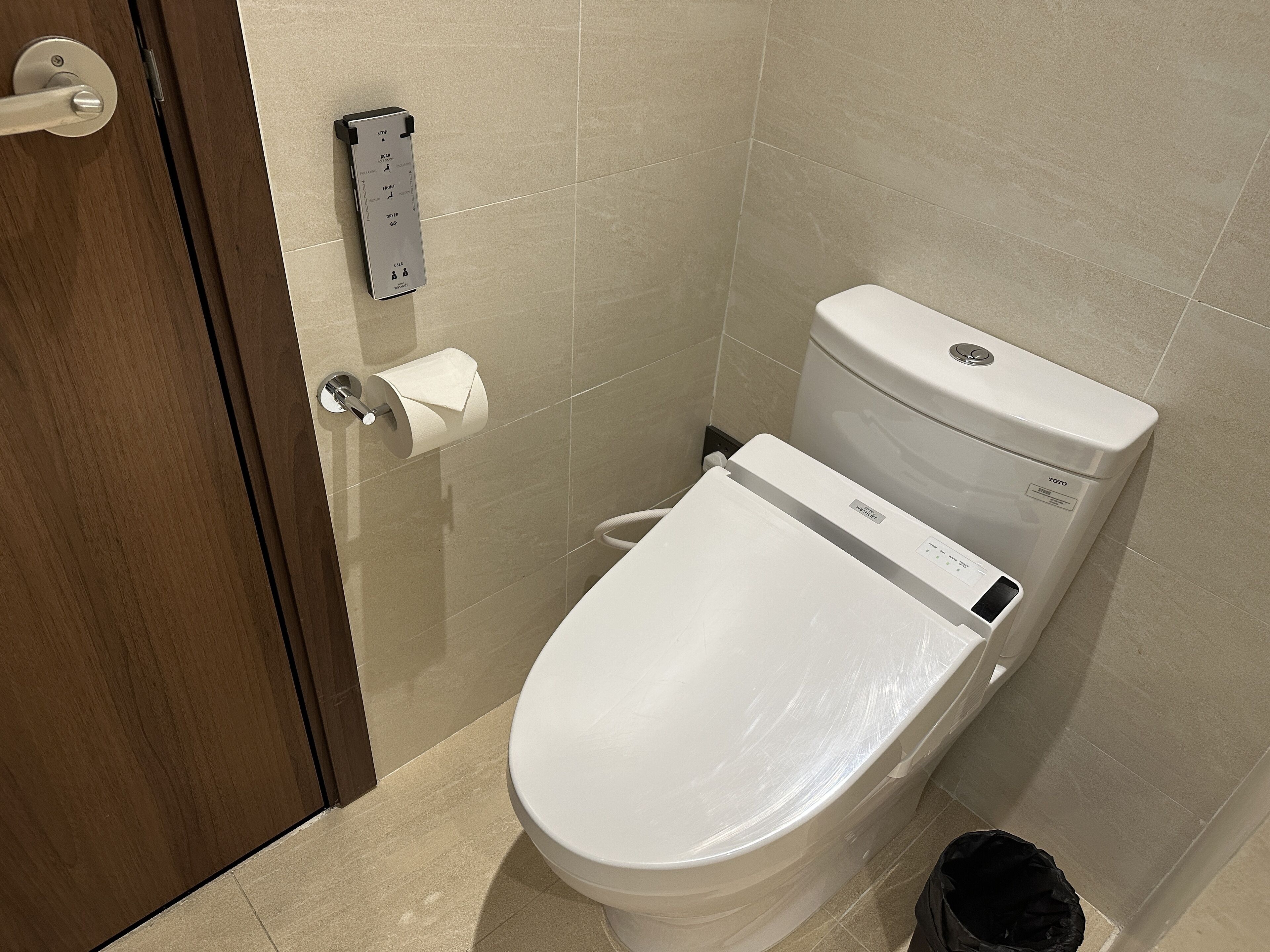 A modern bathroom with a toilet, a paper towel dispenser, and a trash bin.