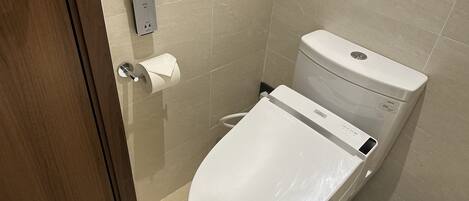 A modern bathroom with a toilet, a paper towel dispenser, and a trash bin.