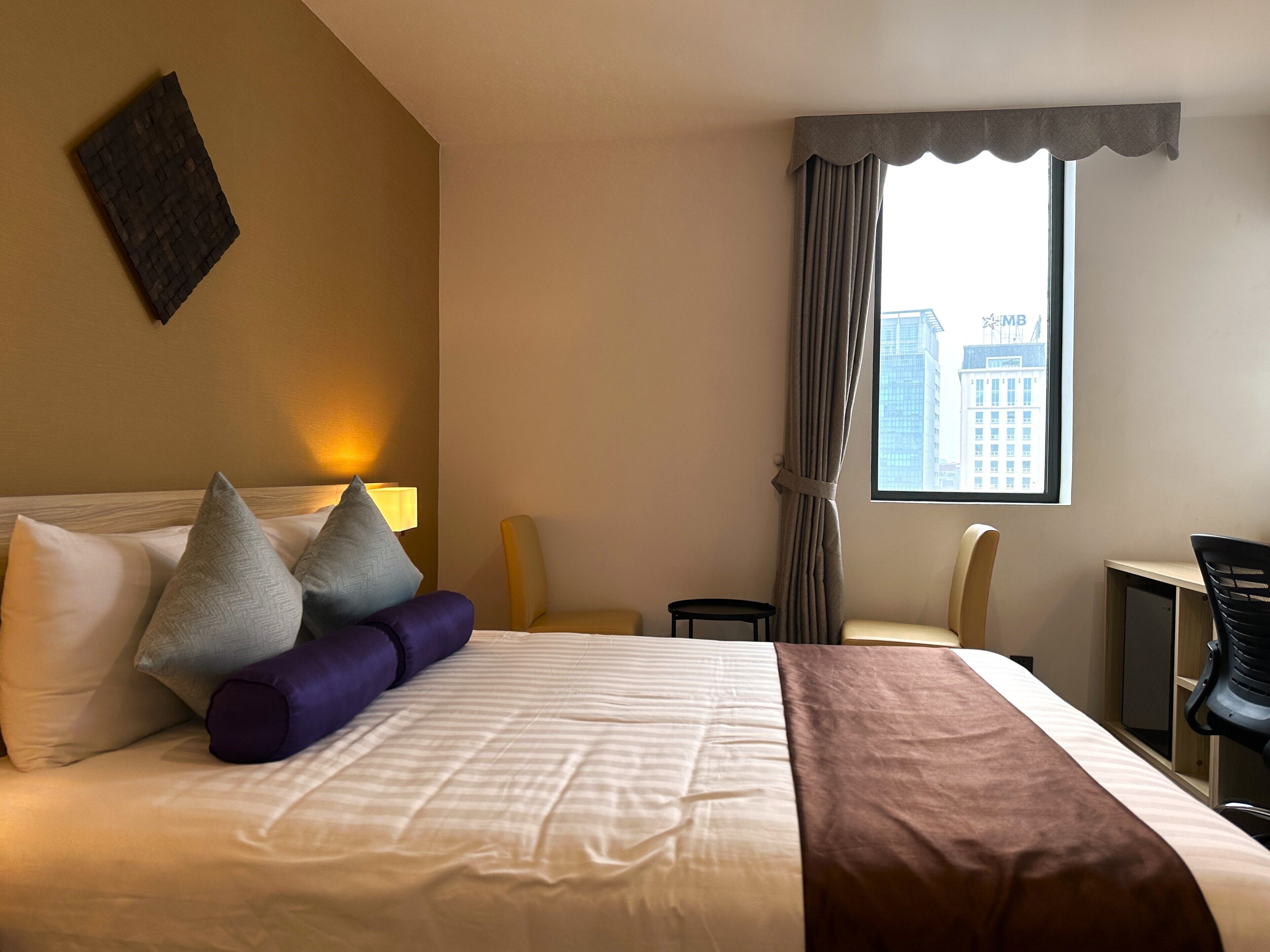 Habitación de hotel con una cama grande, una silla, un escritorio y ventana con vista a la ciudad.