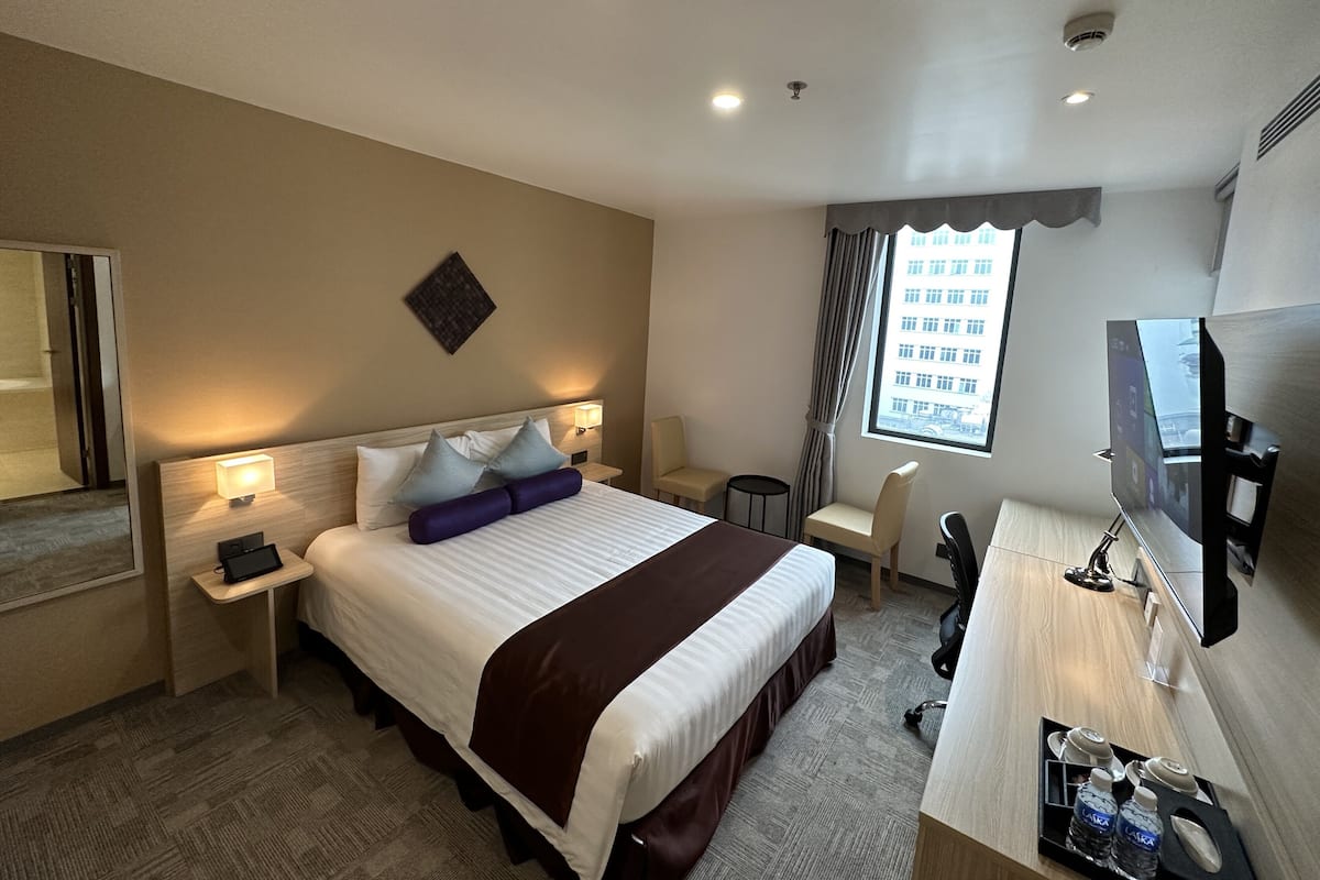 Une chambre d’hôtel avec un grand lit, des tables de chevet, un bureau avec une chaise, une télévision et une fenêtre avec des rideaux.