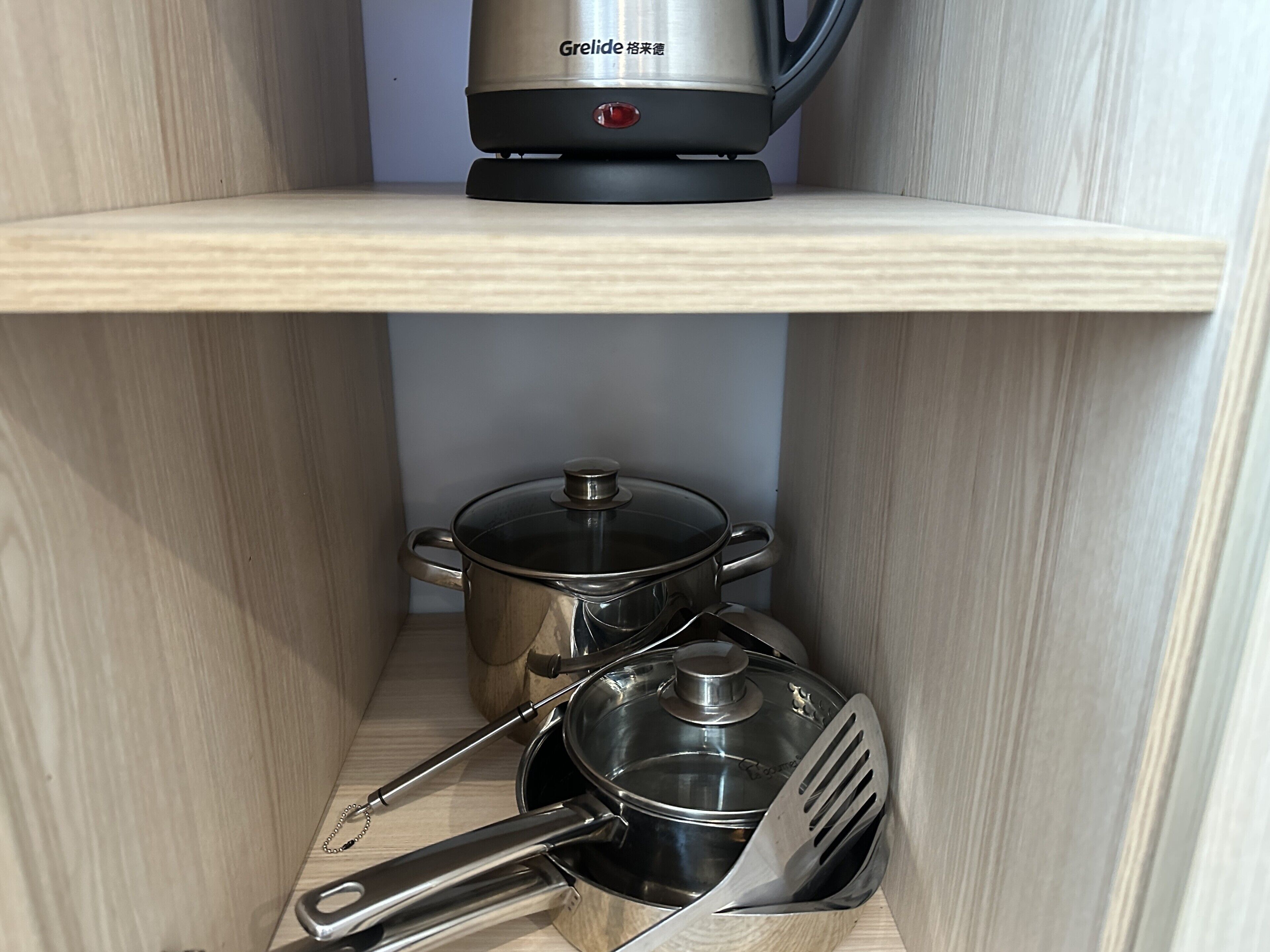Un estante de cocina con una tetera, una olla y una espátula.