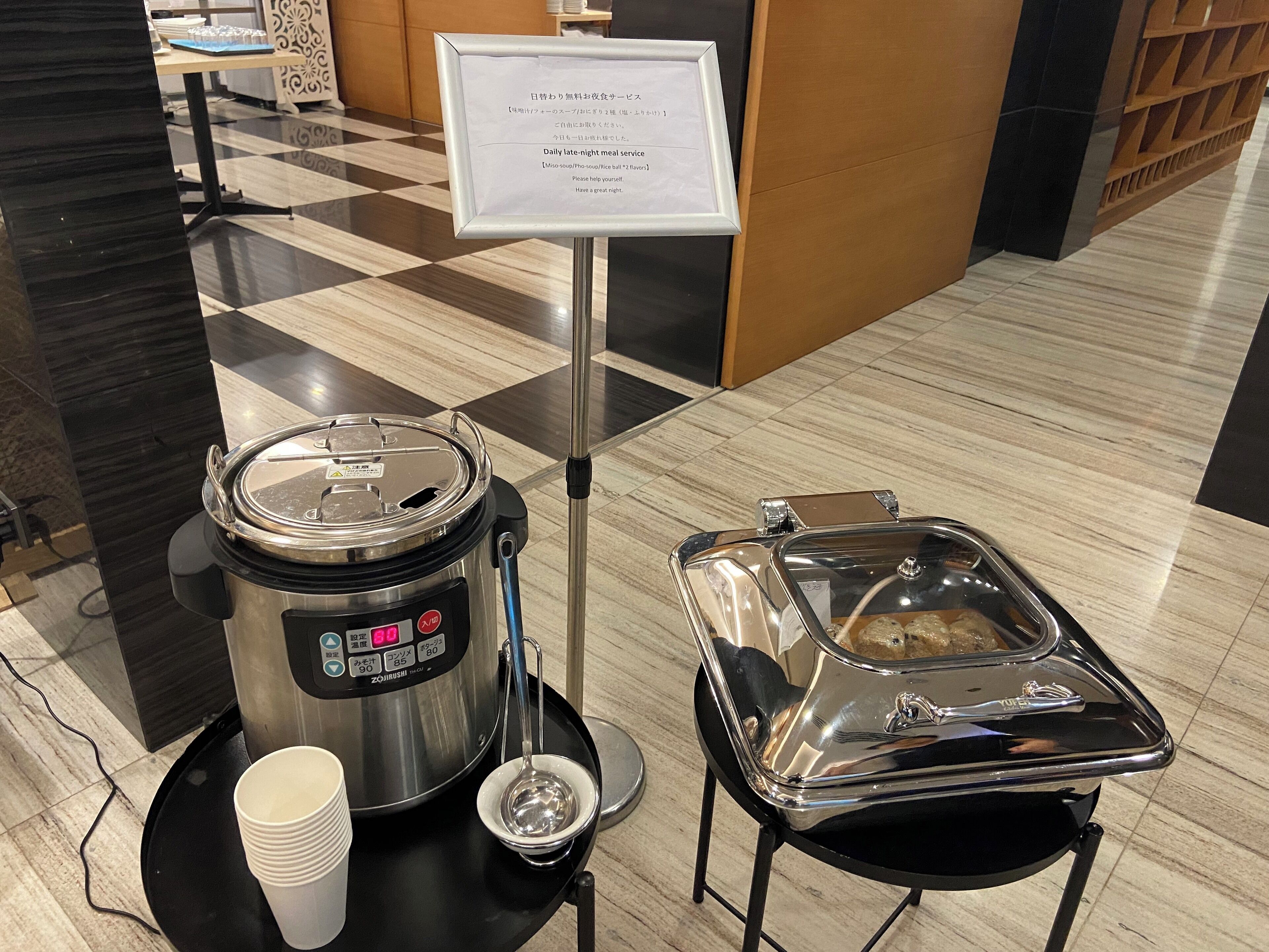 A buffet setup with a hot pot, a soup container, and disposable cups.
