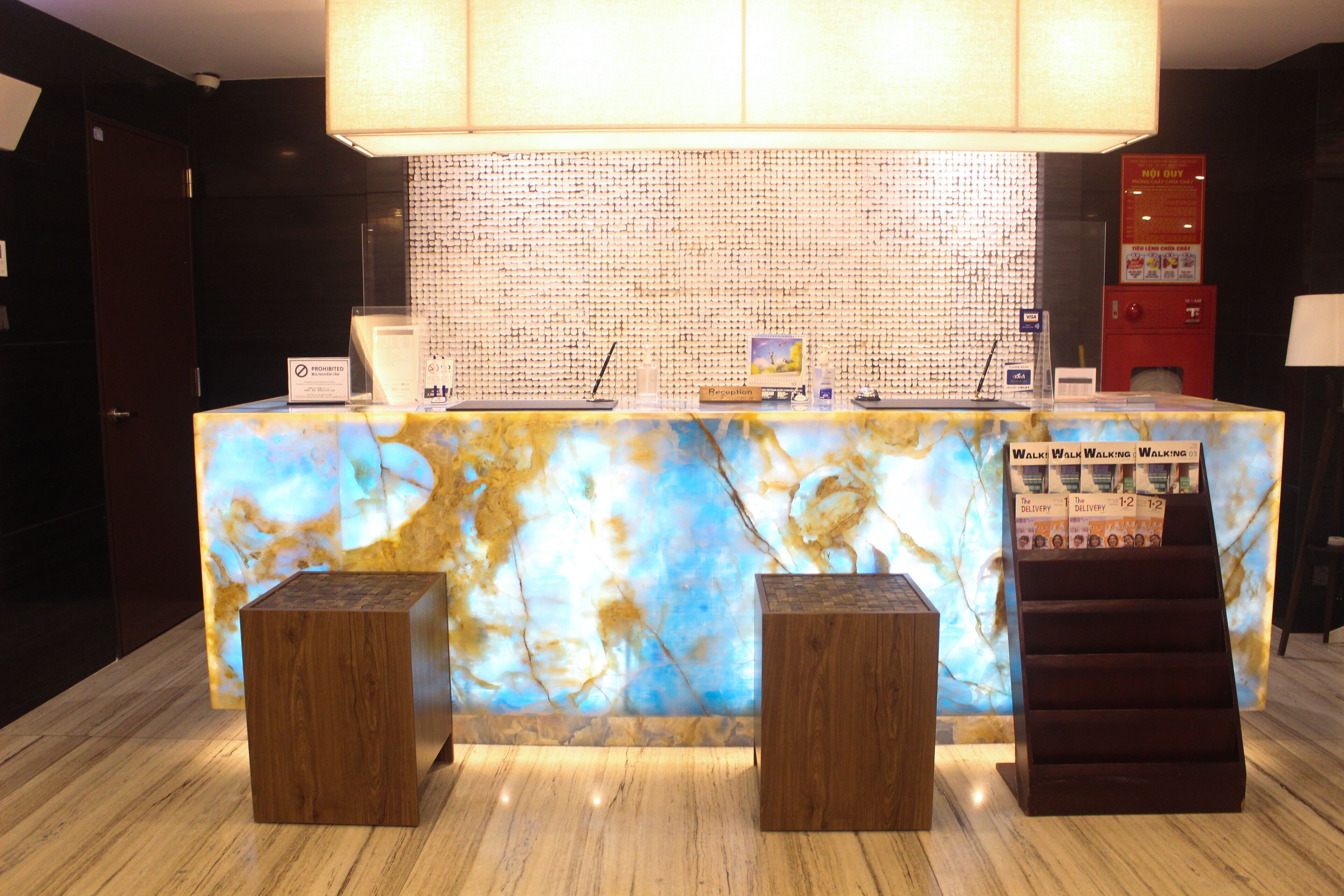 A reception desk with a marble top, two wooden stools, and a red vending machine.