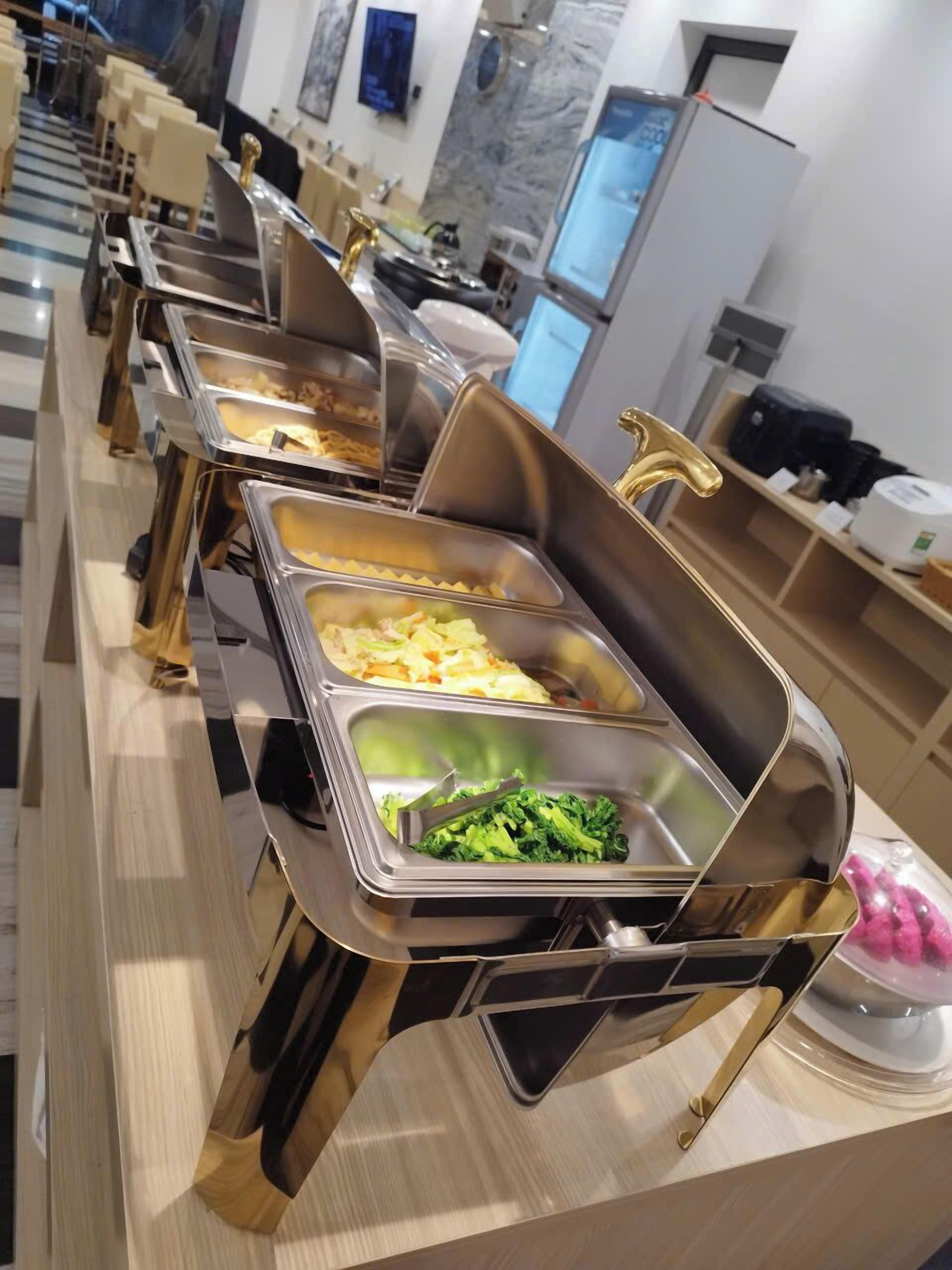 A buffet setup with multiple stainless steel chafing dishes containing various food items, including vegetables and pasta.