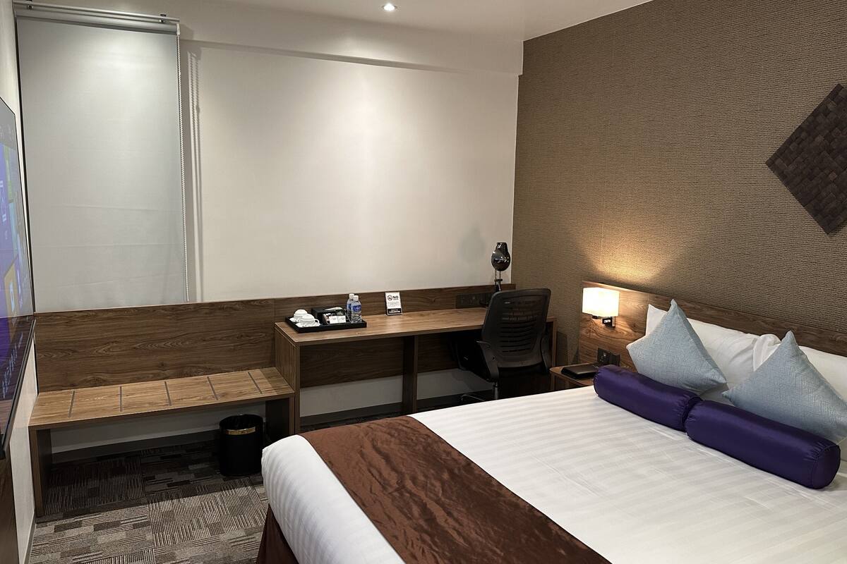 Une chambre d’hôtel équipée d’un lit, d’un bureau, d’une chaise, d’une lampe et d’une poubelle.