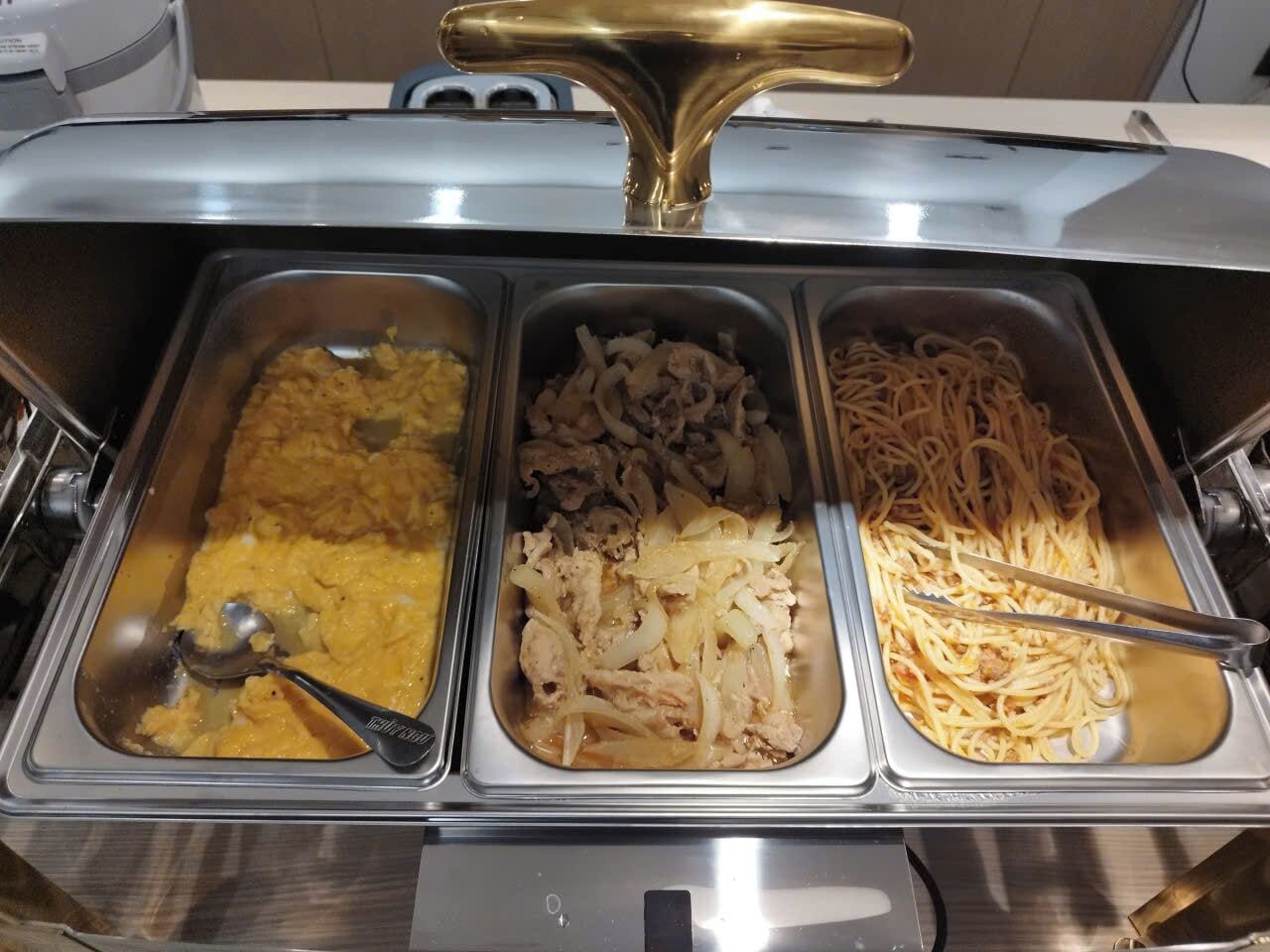 A buffet with three food trays: scrambled eggs, chicken with onions, and spaghetti.