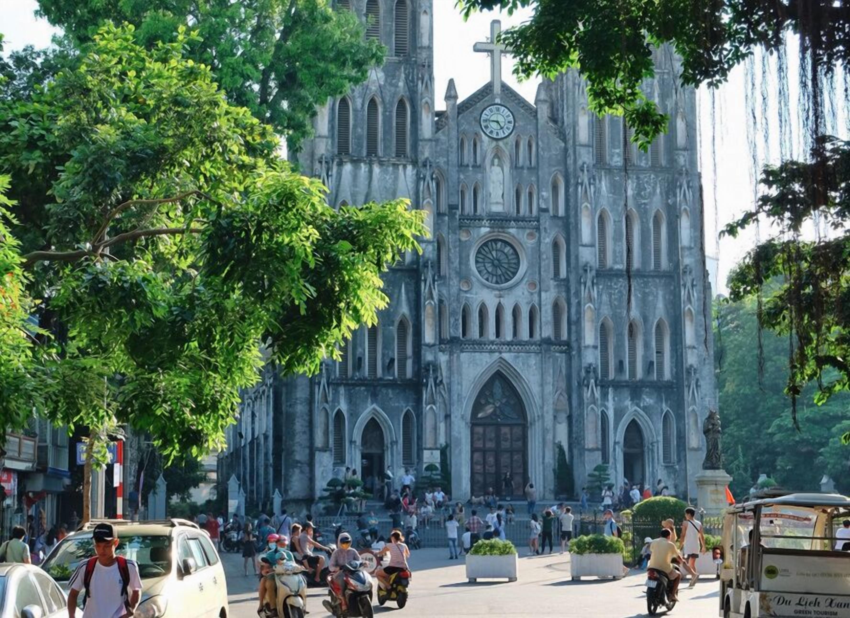 A historic church with a large clock tower, surrounded by trees and busy streets with pedestrians and vehicles.