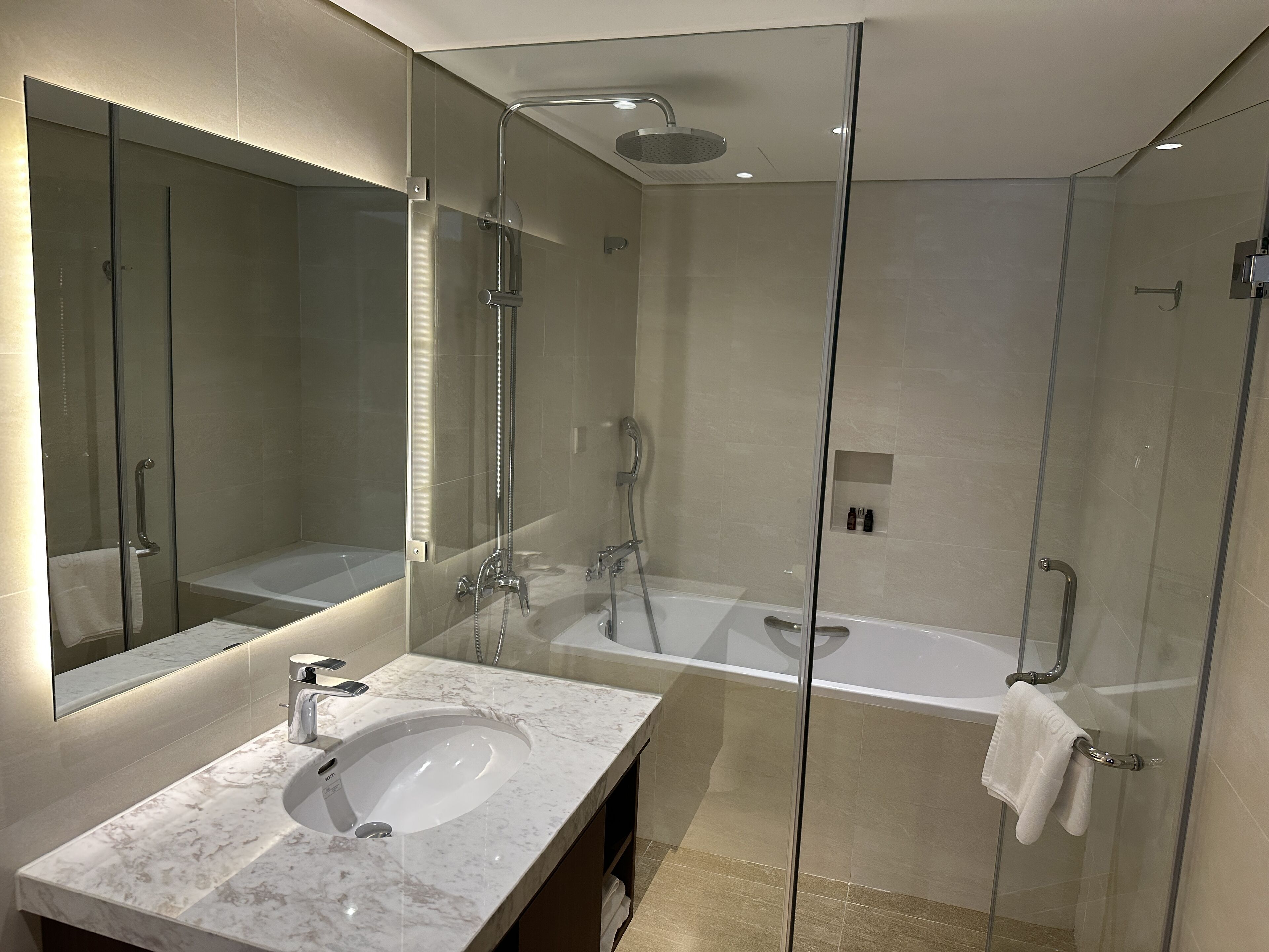A modern bathroom with a glass-enclosed shower, a bathtub, and a marble sink.