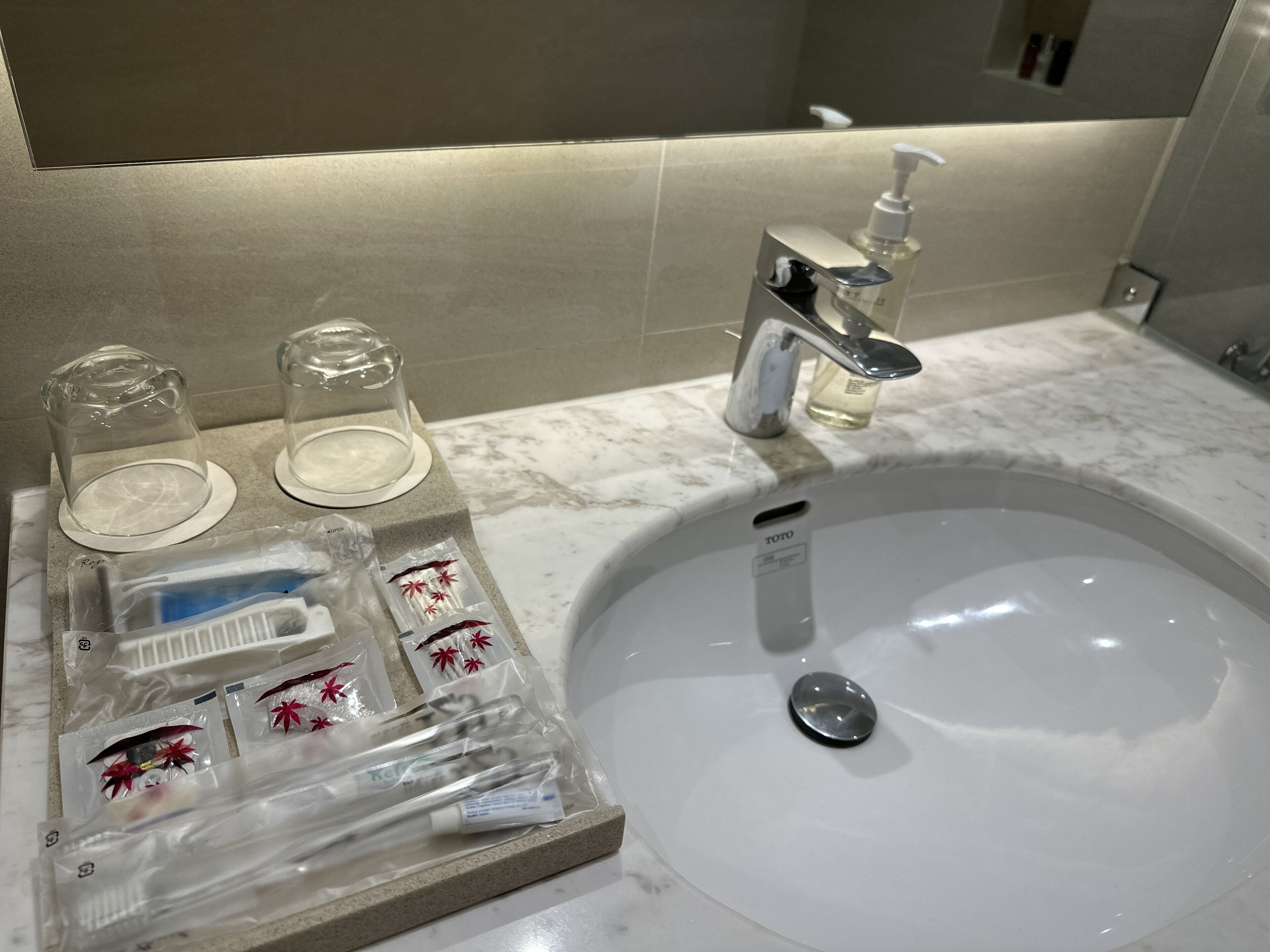 Un bagno con un lavandino bianco, uno specchio, un dispenser di sapone e un vassoio con articoli da toilette.