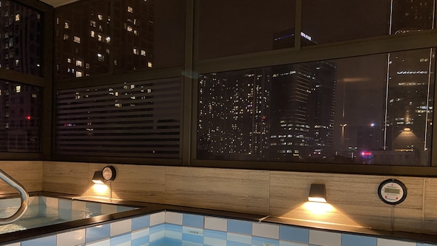 Un baño moderno con piso de azulejos azules, ducha integrada y ventana con vista nocturna a la ciudad.