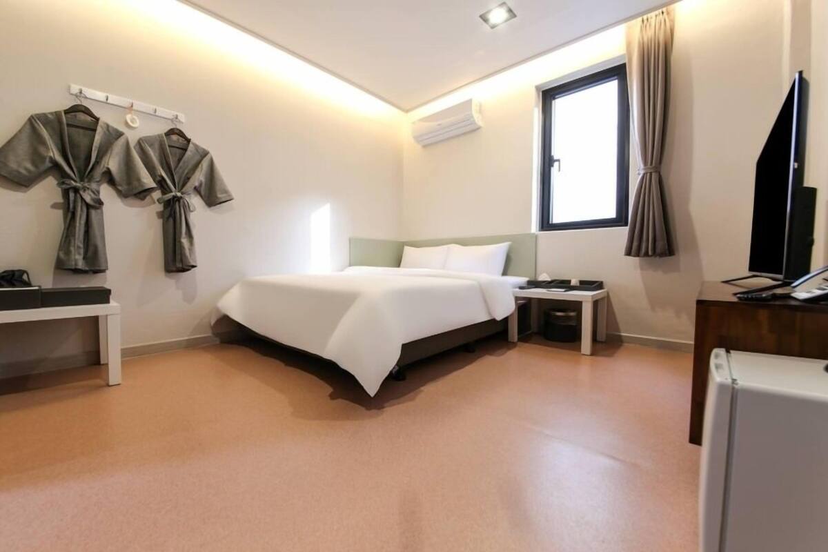 A hotel room with a bed, bedside tables, a desk with a computer, a TV, and a window with curtains.