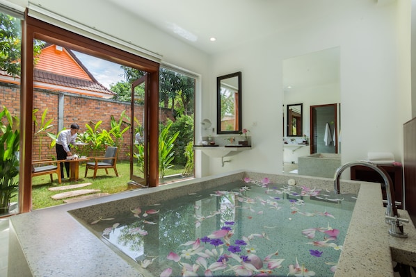A bathroom with a large window, a bathtub filled with water and flowers, and a sink with a mirror above it.
