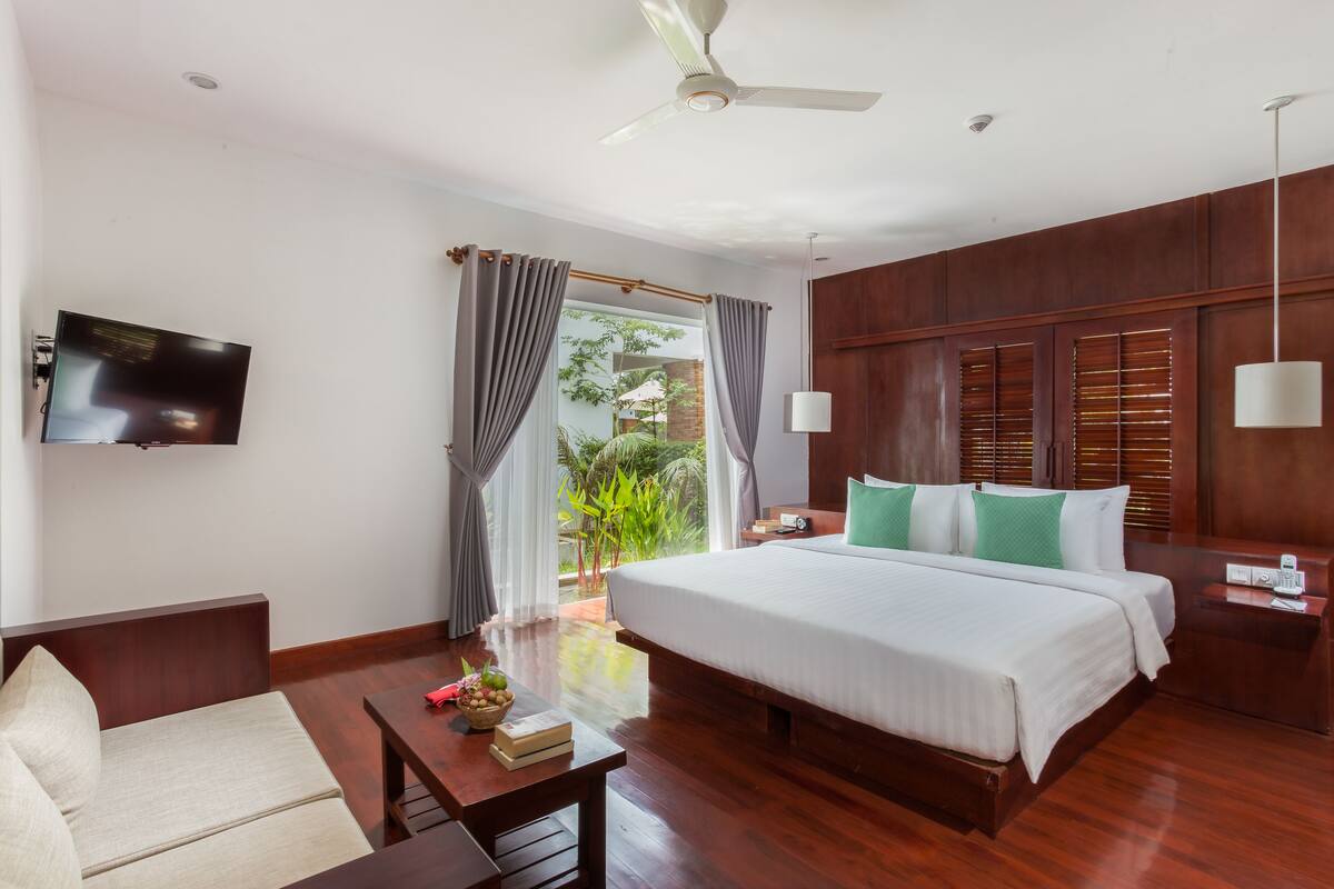 Quarto de hotel com uma cama grande, uma escrivaninha com cadeira, uma TV na parede e vista para o exterior pela janela.