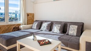 A modern living room with a sofa, a coffee table, and a view of the city through large windows.