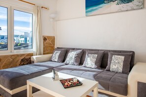 A modern living room with a sofa, a coffee table, and a view of the city through large windows.