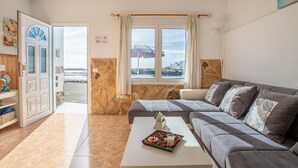 A living room with a sofa, a coffee table with a decorative item, a view of the sea, and a stone wall.