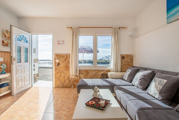 Un salon comprenant un canapé, une table basse agrémentée d’un objet décoratif, une vue sur la mer et un mur en pierre.