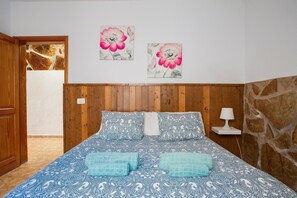 Une chambre à coucher avec une tête de lit en bois, un lit recouvert d’une literie à motifs, deux tableaux accrochés au mur et un mur d’accent en pierre.