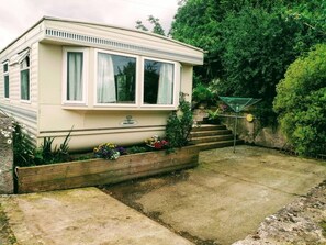 Une maison mobile dotée d’un porche à l’avant, d’un petit jardin agrémenté de fleurs et d’un escalier menant à l’entrée.
