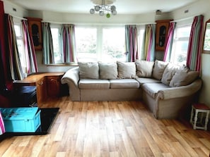 A cozy living room with a beige sectional sofa, wooden flooring, and large windows with colorful curtains.