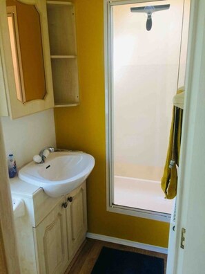Une salle de bain avec un lavabo blanc, un miroir, un porte-serviettes et une douche dotée d’une porte en verre.