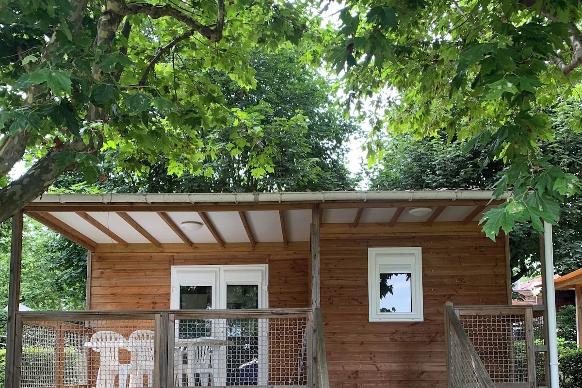 A wooden cabin with a covered porch, a fenced area, and a staircase leading to the entrance.