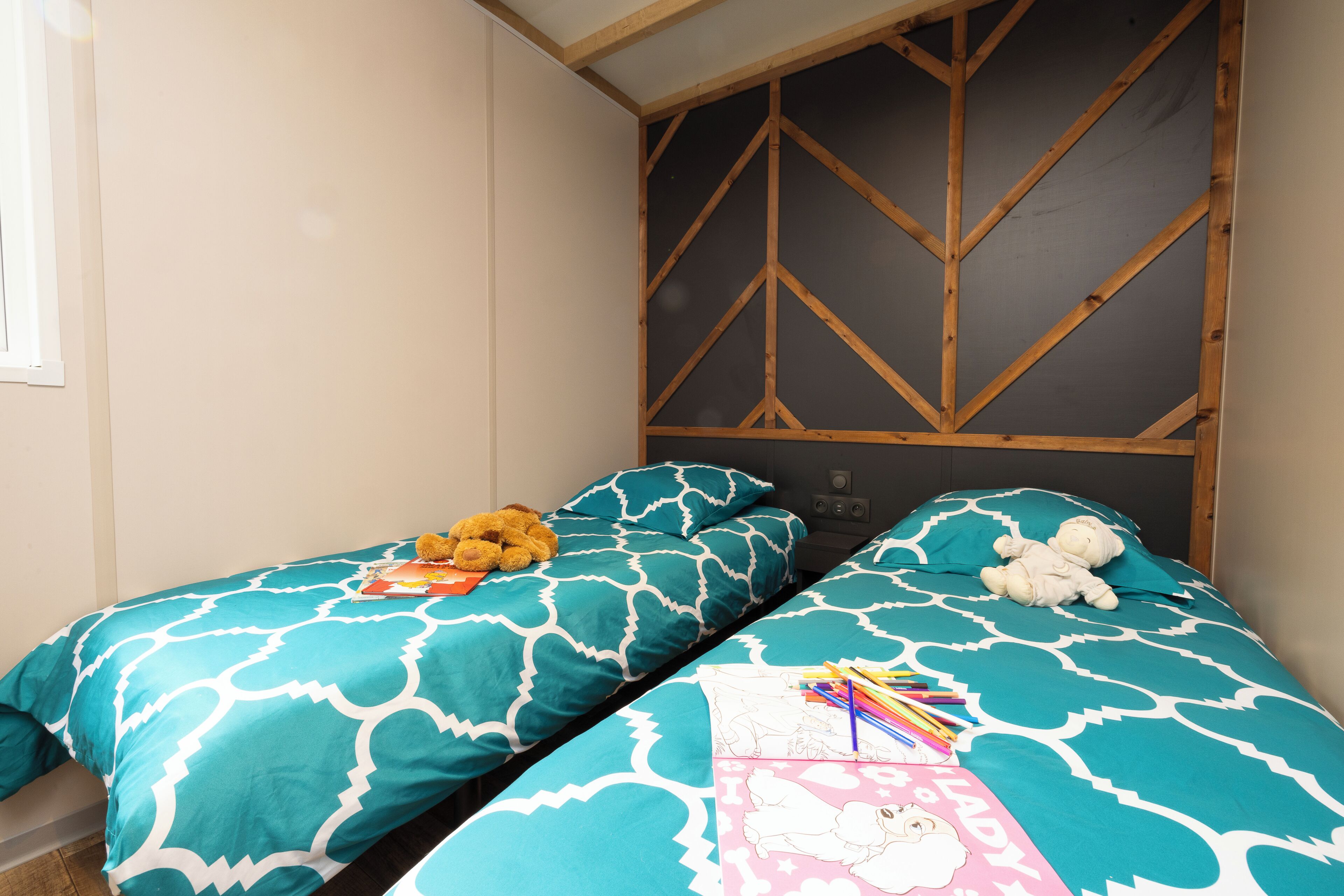A bedroom with two beds, each with a teal patterned bedspread and a pink pillow with a cartoon character.