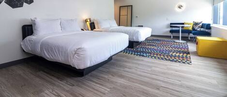 A modern hotel room with two beds, a colorful rug, a yellow ottoman, and a large window.