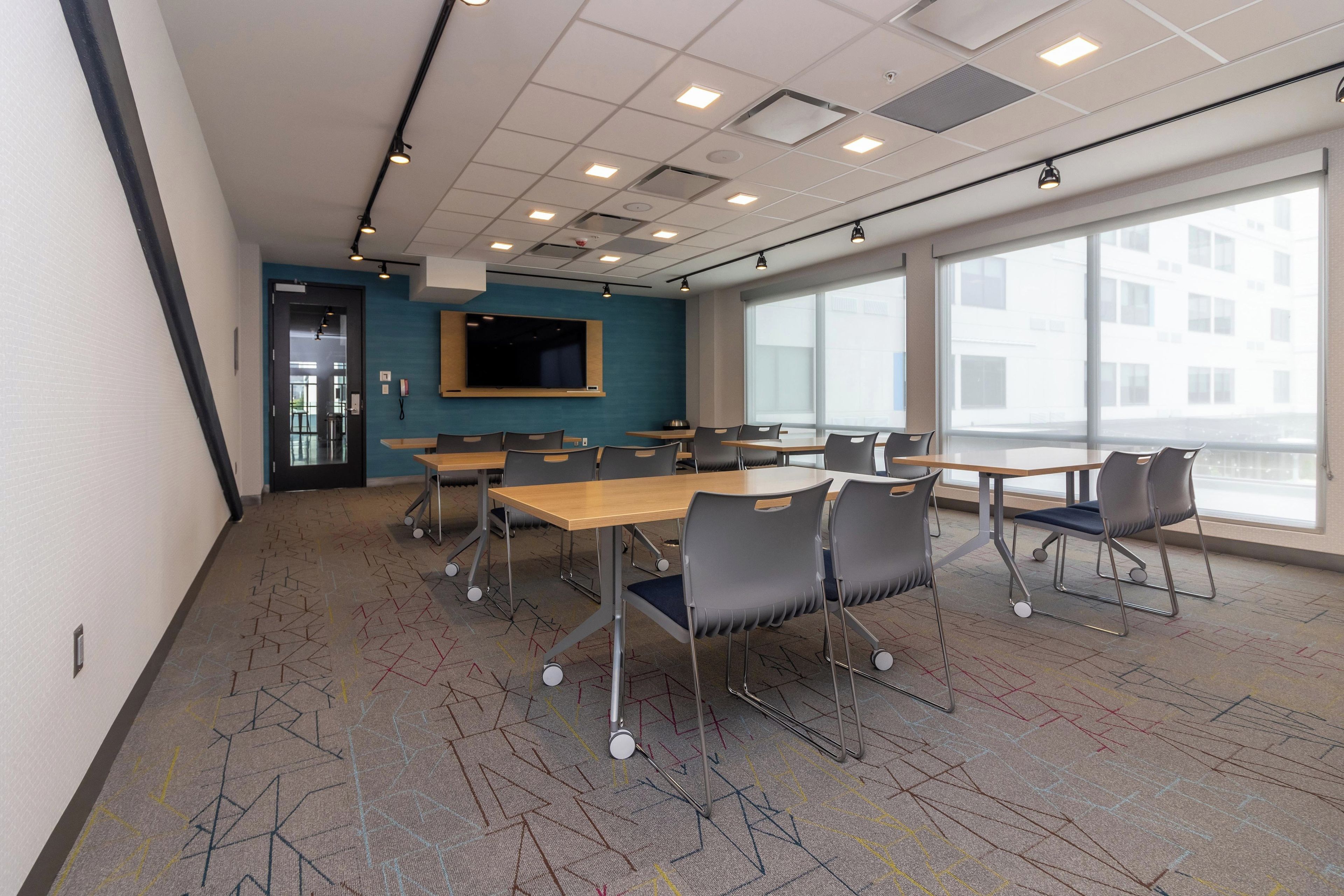 A conference room with tables and chairs, a large window, and a flat-screen TV on the wall.