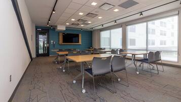A conference room with tables and chairs, a large window, and a flat-screen TV on the wall.