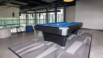 A pool table in a modern indoor setting with a glass railing and a view of the outdoors.