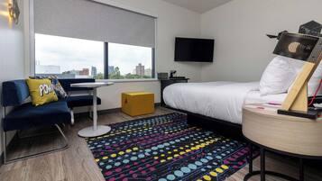Une chambre d’hôtel équipée d’un lit, d’un bureau, d’une chaise, d’une télévision et d’une fenêtre donnant sur la ville.