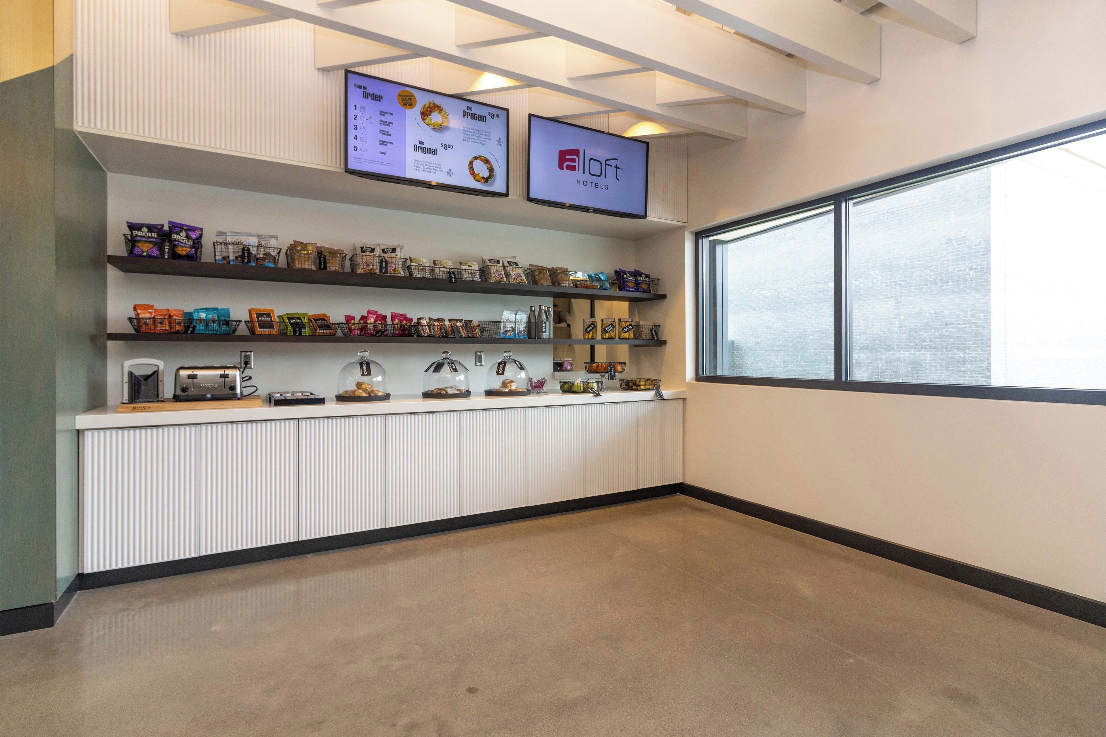 A hotel kitchenette with a menu display, snack shelves, and a window view.
