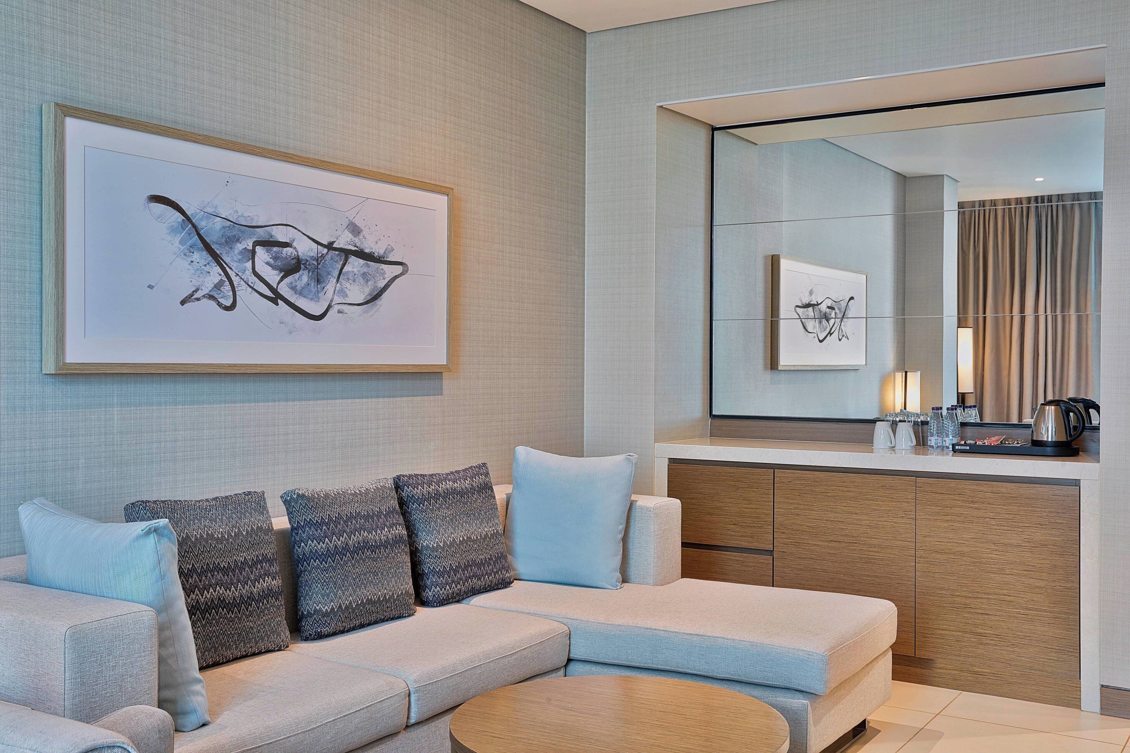 A modern living room with a sofa, a coffee table, and a large mirror reflecting the room.